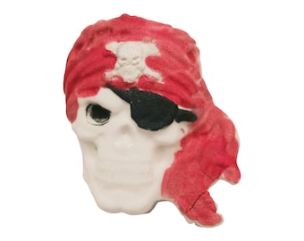 May include: A skull-shaped decorative item with a red bandana and a black eye patch. The bandana has a white skull and crossbones emblem. The skull is white with a detailed facial structure, perfect for Halloween or pirate-themed decor.