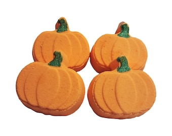 May include: Four pumpkin-shaped bath bombs in a bright orange color. Each bath bomb features a textured, rounded body with vertical ridges and a small, distinct green stem at the top. The surface of the orange pumpkin appears matte.