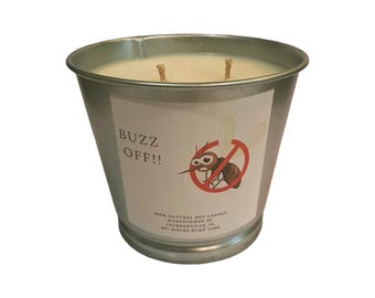 May include: A two-wick soy candle in a silver-colored metal bucket container. The label features the text "BUZZ OFF!!" and a graphic of a mosquito inside a red prohibition circle. Additional text reads "100% NATURAL SOY CANDLE HANDPOURED IN JACKSONVILLE, FL 80+ HOURS BURN TIME."