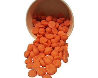 May include: A light-colored paper cup tipped over, spilling a collection of small, bright orange wax melts. The wax pieces are a mix of smooth, circular discs and detailed, molded pumpkin shapes, all in a uniform, vibrant orange color.