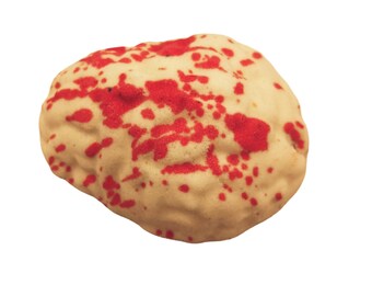 May include: A round, textured, off-white cookie or confection featuring irregular, vibrant red splatters across its surface. The object has a bumpy, uneven exterior with a dense, rounded shape, resembling a brain-like structure in its form.