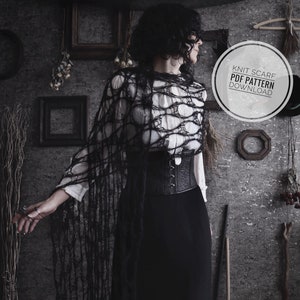 Puede incluir: Una mujer lleva una bufanda de punto negra con un borde deshilachado. La bufanda está drapeada sobre una camisa blanca y una falda negra. La mujer está de pie frente a una pared con un marco de madera y un cartel que dice "Knit Scarf PDF Pattern Download".