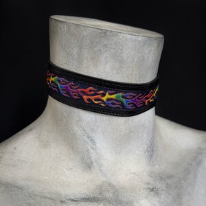 Rainbow flame print jacquard ribbon upper sewn onto a one inch wide black faux vegan leather choker collar base. Piece is adjustable and closes in back with a black metal hook. Tags lgbtq pride month queer gay goth flamer ribbon necklace punk rock