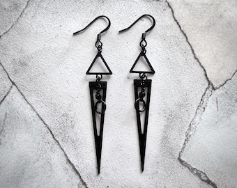 May include: A pair of black triangle earrings with a dangling geometric design. The earrings have a hook closure.