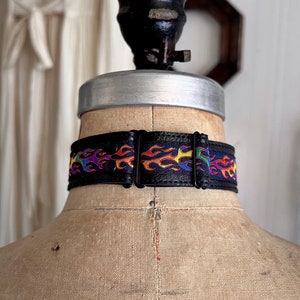 Rainbow flame print jacquard ribbon upper sewn onto a one inch wide black faux vegan leather choker collar base. Piece is adjustable and closes in back with a black metal hook. Tags lgbtq pride month queer gay goth flamer ribbon necklace punk rock