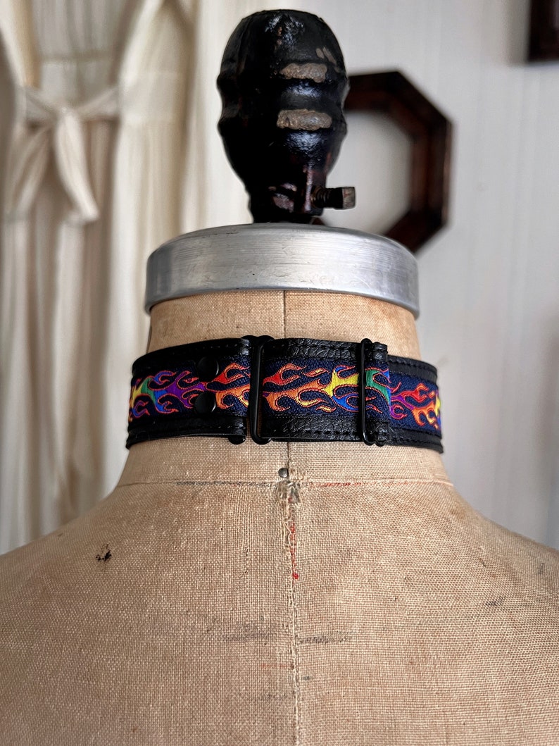 Rainbow flame print jacquard ribbon upper sewn onto a one inch wide black faux vegan leather choker collar base. Piece is adjustable and closes in back with a black metal hook. Tags lgbtq pride month queer gay goth flamer ribbon necklace punk rock