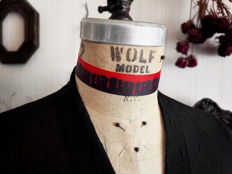 May include: A black choker necklace with a red ribbon and black dripping paint design. The choker is on a mannequin's neck. The mannequin is labelled "Wolf Model".