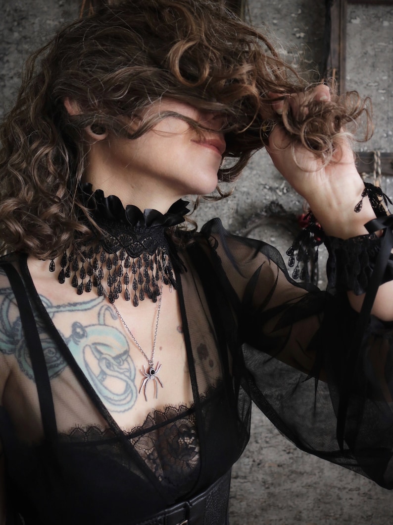 A wide black lace choker collar encircles the neck. Lace is detailed, textured and falls in dainty teardrop fringe past the collarbones. Choker is topped with wide black satin pleated trim. Tags romantic gothic dark fashion vampire wedding mourning