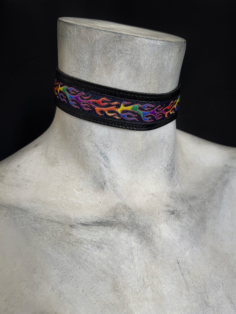 Rainbow flame print jacquard ribbon upper sewn onto a one inch wide black faux vegan leather choker collar base. Piece is adjustable and closes in back with a black metal hook. Tags lgbtq pride month queer gay goth flamer ribbon necklace punk rock
