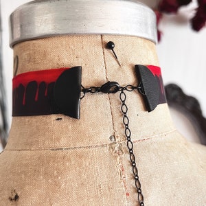 Picture shows a wide black grosgrain ribbon choker necklace with dark red blood drops running down collar. Piece closes in back with a lobster clasp and Figaro extender chain. Tags vampire collar, halloween choker, gothic Dracula, plus size available