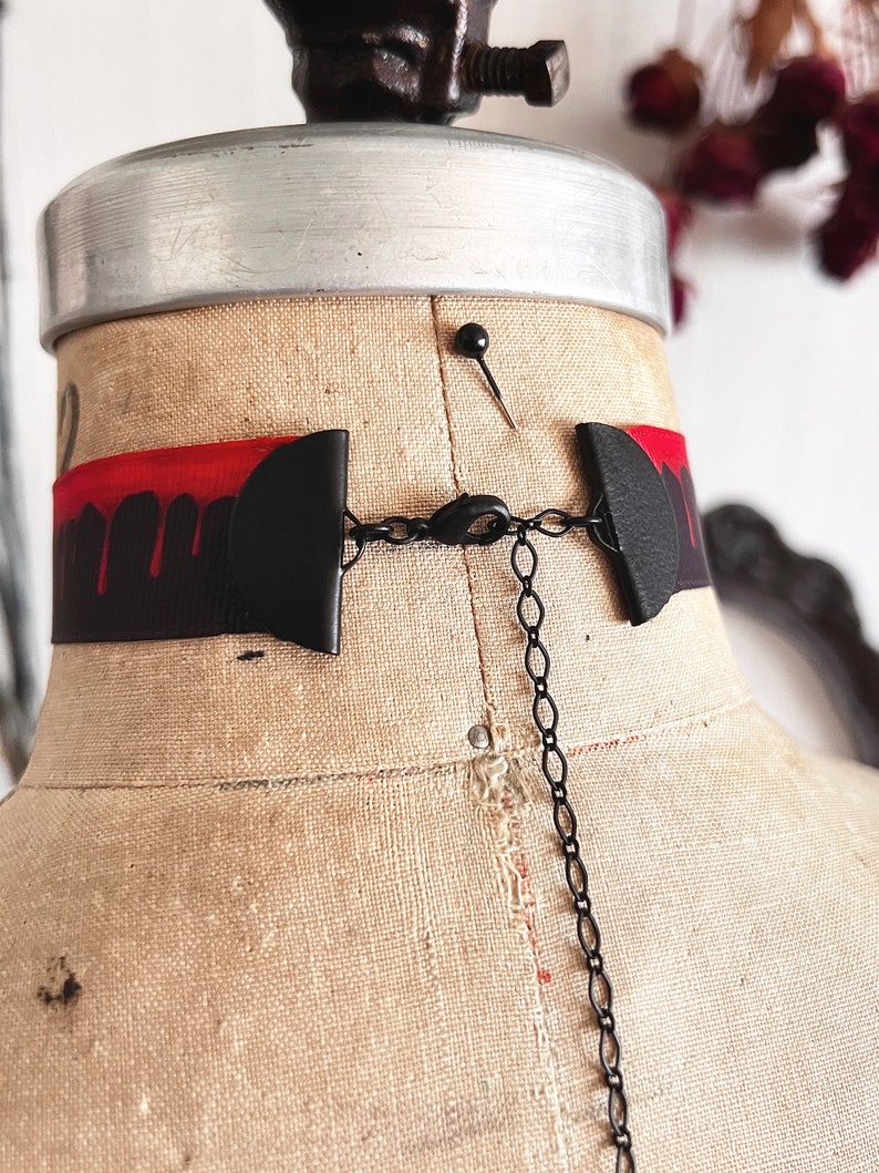 Picture shows a wide black grosgrain ribbon choker necklace with dark red blood drops running down collar. Piece closes in back with a lobster clasp and Figaro extender chain. Tags vampire collar, halloween choker, gothic Dracula, plus size available