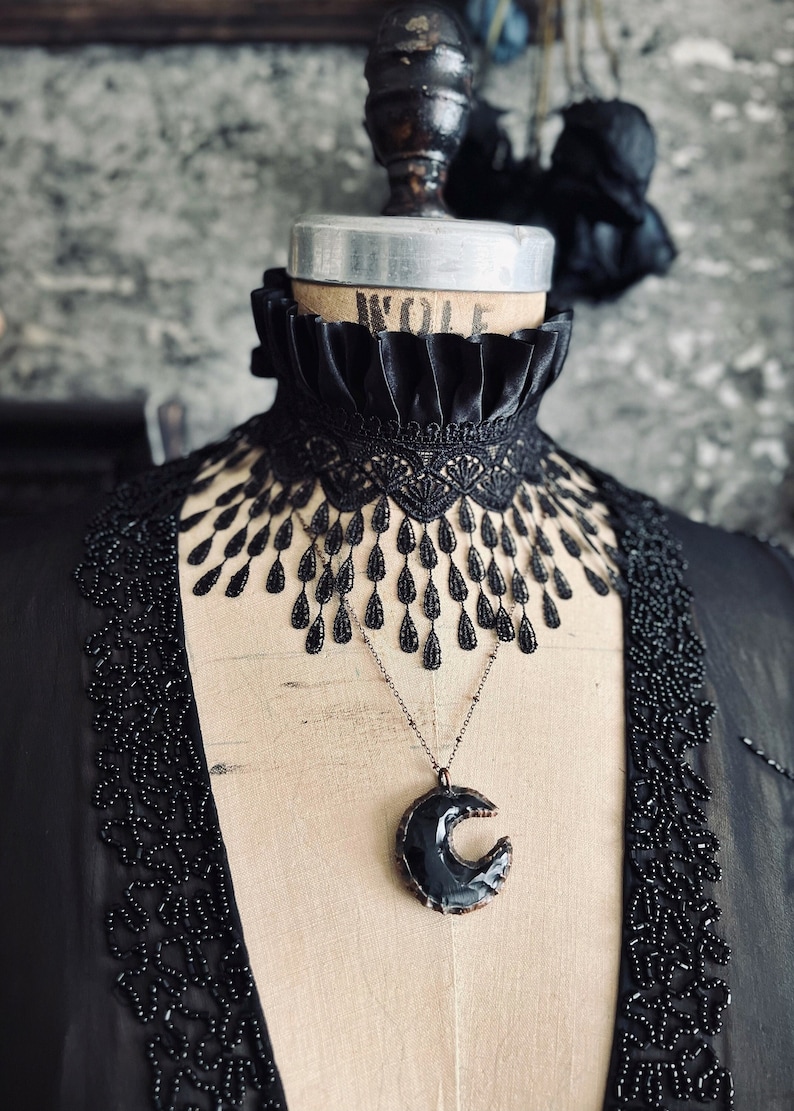 A wide black lace choker collar encircles the neck. Lace is detailed, textured and falls in dainty teardrop fringe past the collarbones. Choker is topped with wide black satin pleated trim. Tags romantic gothic dark fashion vampire wedding mourning