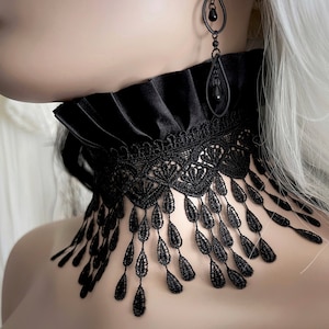 A wide black lace choker collar encircles the neck. Lace is detailed, textured and falls in dainty teardrop fringe past the collarbones. Choker is topped with wide black satin pleated trim. Tags romantic gothic dark fashion vampire wedding mourning