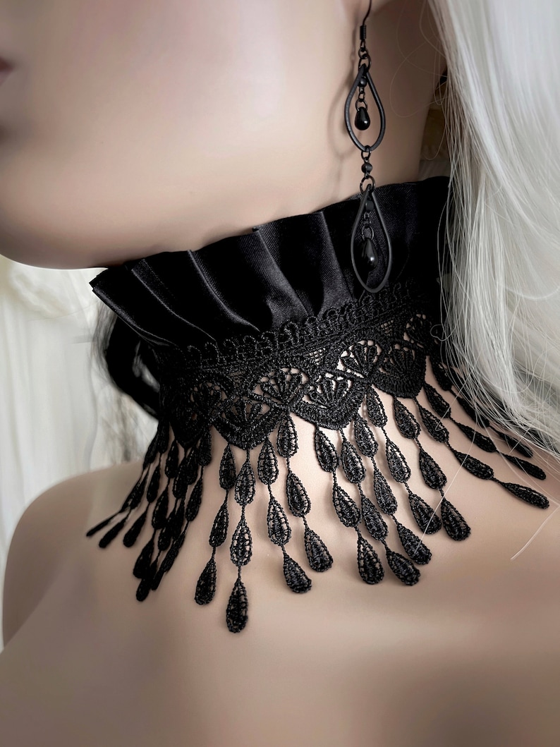 A wide black lace choker collar encircles the neck. Lace is detailed, textured and falls in dainty teardrop fringe past the collarbones. Choker is topped with wide black satin pleated trim. Tags romantic gothic dark fashion vampire wedding mourning