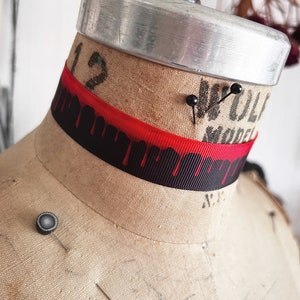 Picture shows a wide black grosgrain ribbon choker necklace with dark red blood drops running down collar. Piece closes in back with a lobster clasp and Figaro extender chain. Tags vampire collar, halloween choker, gothic Dracula, plus size available