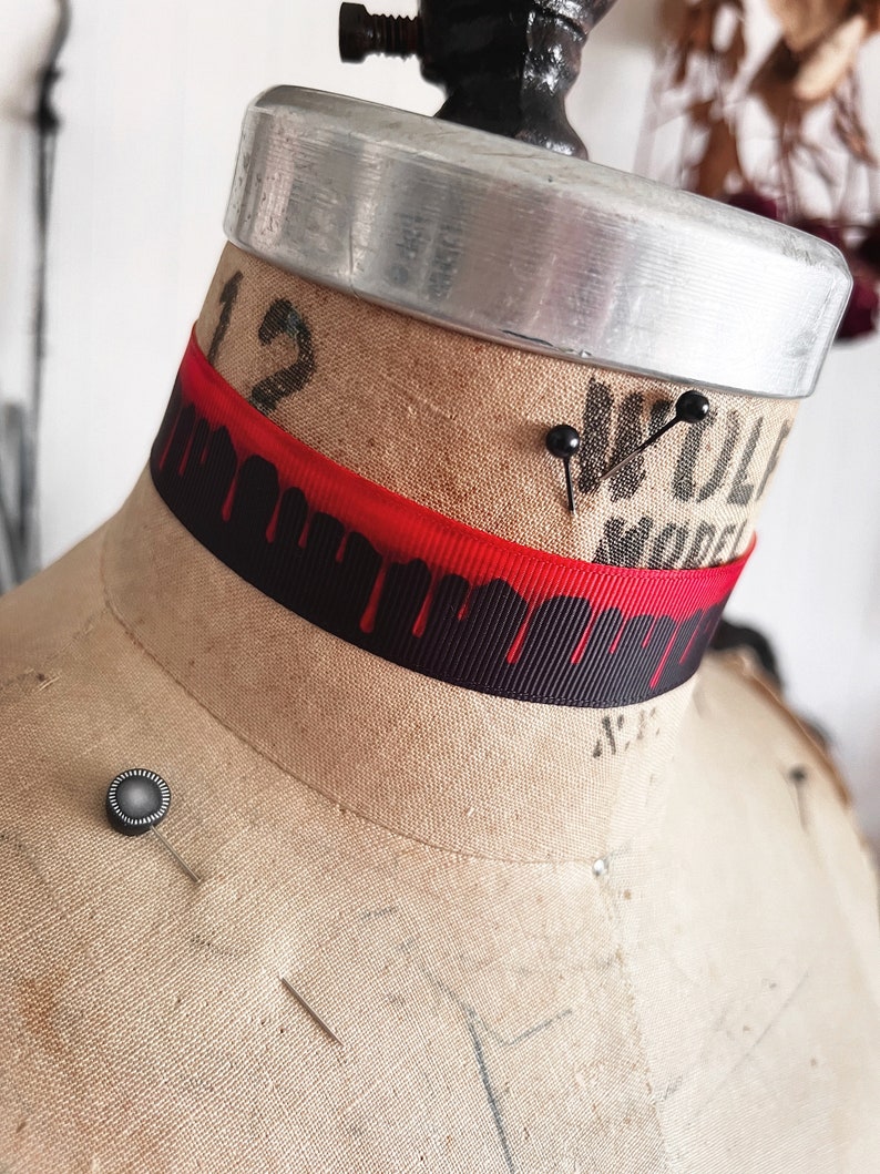 Picture shows a wide black grosgrain ribbon choker necklace with dark red blood drops running down collar. Piece closes in back with a lobster clasp and Figaro extender chain. Tags vampire collar, halloween choker, gothic Dracula, plus size available