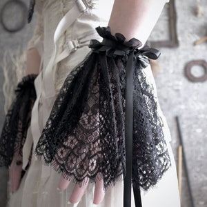 May include: Black lace wrist cuffs with a black satin ribbon. The cuffs are gathered at the wrist and have a delicate lace pattern.