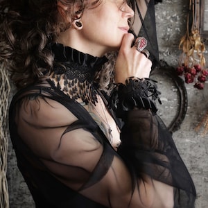 A wide black lace choker collar encircles the neck. Lace is detailed, textured and falls in dainty teardrop fringe past the collarbones. Choker is topped with wide black satin pleated trim. Tags romantic gothic dark fashion vampire wedding mourning