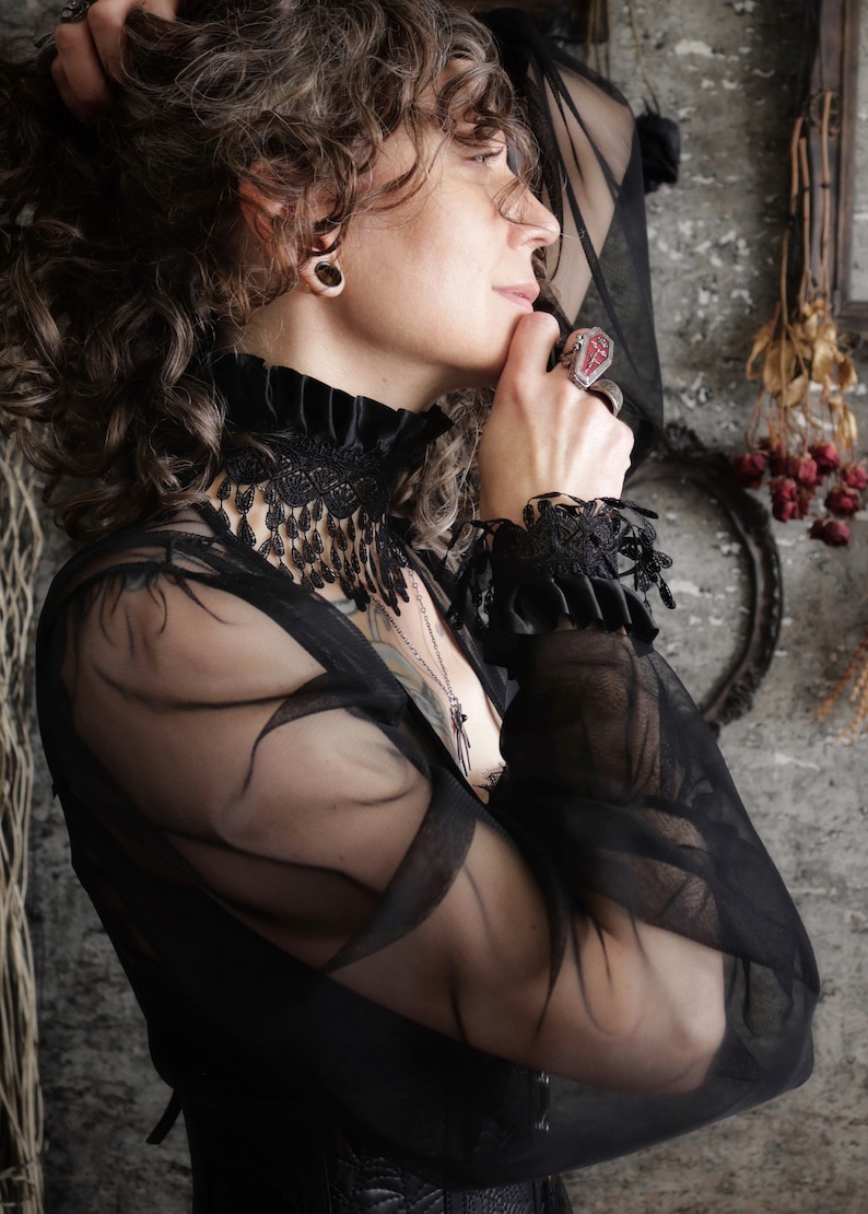 A wide black lace choker collar encircles the neck. Lace is detailed, textured and falls in dainty teardrop fringe past the collarbones. Choker is topped with wide black satin pleated trim. Tags romantic gothic dark fashion vampire wedding mourning