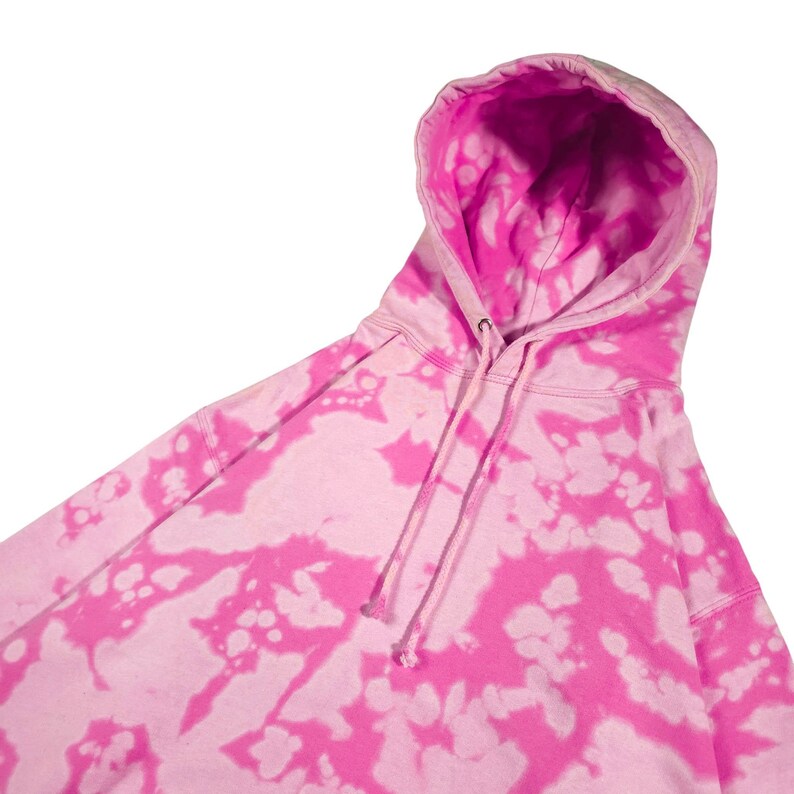 Puede incluir: Una sudadera con capucha rosa te&ntilde;ida con un cord&oacute;n. La sudadera tiene una base rosa claro con un vibrante estampado tie-dye rosa. El interior de la capucha es de color rosa brillante liso. La prenda est&aacute; hecha de un material suave.
