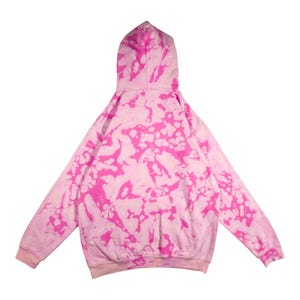 Puede incluir: Una sudadera con capucha rosa y blanca con te&ntilde;ido anudado, con capucha y mangas largas. La vista trasera de la sudadera muestra un patr&oacute;n de manchas rosas sobre un fondo blanco. Los pu&ntilde;os y el dobladillo inferior son de color rosa liso.