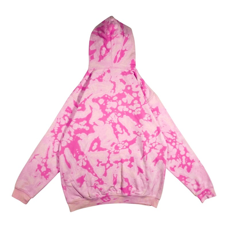 Puede incluir: Una sudadera con capucha rosa y blanca con te&ntilde;ido anudado, con capucha y mangas largas. La vista trasera de la sudadera muestra un patr&oacute;n de manchas rosas sobre un fondo blanco. Los pu&ntilde;os y el dobladillo inferior son de color rosa liso.