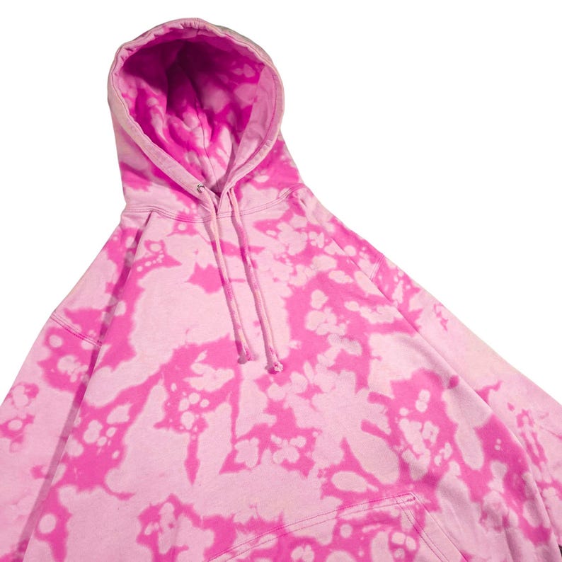 Puede incluir: Una sudadera con capucha rosa te&ntilde;ida con un cord&oacute;n y un bolsillo de canguro. La sudadera tiene una base rosa claro con vibrantes patrones de te&ntilde;ido anudado rosa. El interior de la capucha es de color rosa brillante.