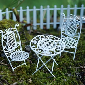 May include: White metal garden furniture set with a round table and two chairs. The set is on a bed of green moss.