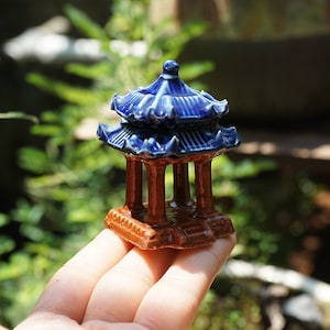 May include: A small blue and brown ceramic pagoda figurine. The pagoda has a tiered roof and four pillars.