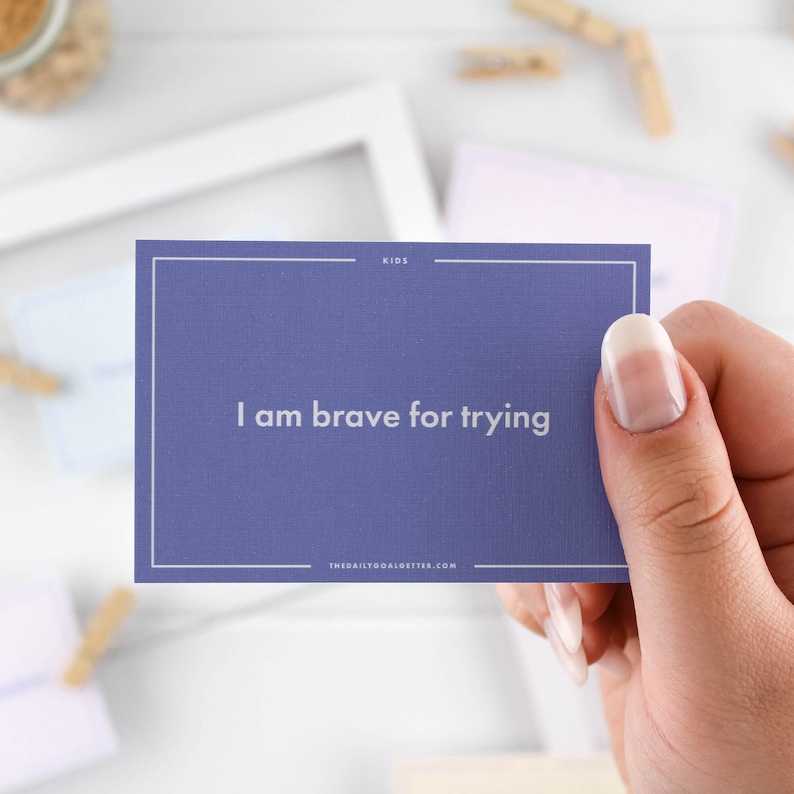 May include: Purple affirmation card with white text that reads "I am brave for trying" and the website "thedailygoalgetter.com". The card is part of a set for kids.