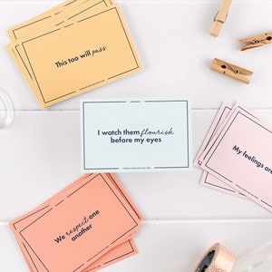 May include: A set of affirmation cards for parents. The cards are printed on different colored paper with black text. The text on the cards includes phrases like "This too will pass" and "We respect one another".