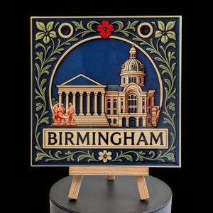 May include: Square ceramic tile with a detailed illustration of a building with a dome, columns, and the word "BIRMINGHAM". The tile is framed with floral and scroll designs in green and cream against a dark blue background. It is displayed on a small wooden easel.