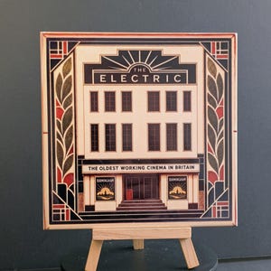 May include: A square decorative tile featuring a graphic illustration of The Electric cinema in Birmingham. The design includes the text THE ELECTRIC and THE OLDEST WORKING CINEMA IN BRITAIN, framed by black, red, and gold geometric leaf patterns.