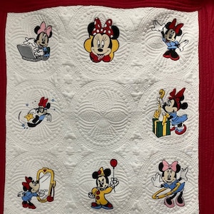 May include: A white quilt with a red border features nine embroidered images of Mickey Mouse and Minnie Mouse in various poses. The quilt is made of cotton fabric and has a quilted design.