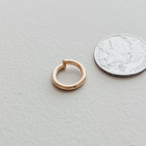 May include: A gold-colored hoop earring with a small gap in the circle. The earring is about the size of a US quarter.