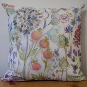 Puede incluir: Una funda de cojín blanca con un estampado floral de acuarela con flores y hojas rosas, moradas y verdes.