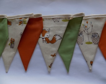 May include: A bunting with a woodland theme. The bunting is made of fabric and has a cream background with brown, orange, and green accents. The bunting features owls, foxes, mushrooms, and leaves.