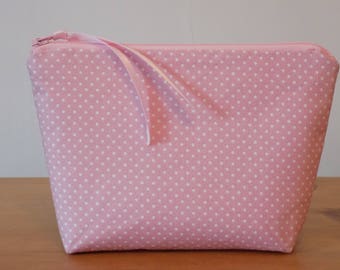 May include: A pink zippered pouch with a white polka dot pattern. The pouch has a white ribbon attached to the zipper.