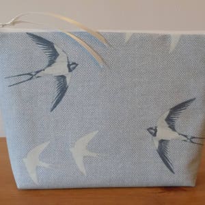 May include: A light blue zippered pouch with a white zipper pull and a pattern of white swallows on a light blue background.