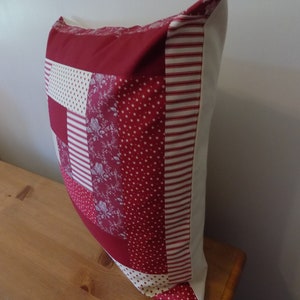 Puede incluir: Almohada de patchwork rojo y blanco con un borde blanco. La almohada est&aacute; hecha de diferentes telas con varios patrones, incluyendo rayas, lunares y dise&ntilde;os florales.