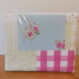 May include: A patchwork fabric zippered pouch with a white ribbon pull. The pouch has a blue and white polka dot pattern, a pink and white gingham pattern, a green and white floral pattern, and a white and beige striped pattern.