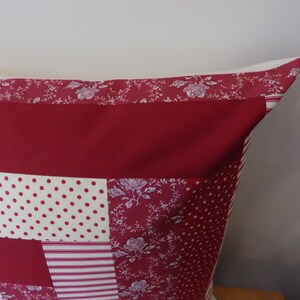Puede incluir: Una almohada de patchwork rojo, blanco y crema con un patr&oacute;n floral. La almohada est&aacute; hecha de diferentes telas y tiene una forma cuadrada.