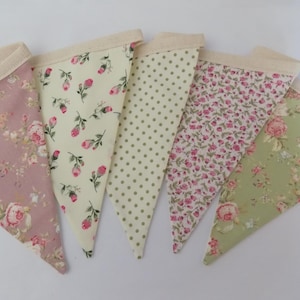 May include: A set of five triangular fabric bunting flags attached to a cream-coloured header tape. The flags feature various patterns including pink roses on mauve, rosebuds on cream, green polka dots, small pink floral prints, and pink roses on sage.