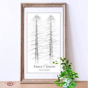 May include: Framed art print featuring a pencil drawing of two tall trees. The artwork is in black and white, with the names "Emily & David" and the date "10.10.2019" printed below the trees. The frame is a light brown color.