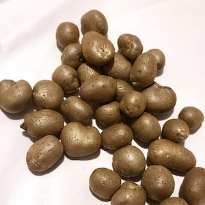 May include: A collection of brown, irregularly shaped yam-like tubers, possibly Dioscorea bulbifera, scattered on a white surface. The tubers have a rough, textured surface and vary in size, with some showing small protrusions.