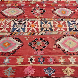 May include: A red, black, white, blue, and pink patterned rug with a geometric design. The rug has a fringe border.