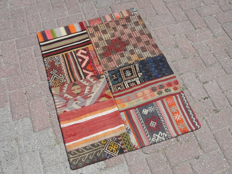 May include: A patchwork rug with a variety of colorful geometric patterns and designs. The rug is made of woven fabric and has a rustic, vintage look.