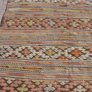 K&ouml;nnte beinhalten: Ein rechteckiger Teppich mit geometrischem Muster in Braun-, Orange- und Cremet&ouml;nen. Das Design des Teppichs umfasst Rauten- und Streifenmotive. Er besteht aus gewebtem Material, wodurch er sich strukturiert anf&uuml;hlt.