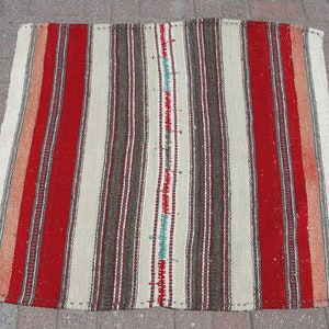 May include: A rectangular woven rug featuring vertical stripes in red, cream, brown, and orange. The rug has a central cream stripe with turquoise accents. The rug is likely made of natural fibres and is suitable for indoor use.