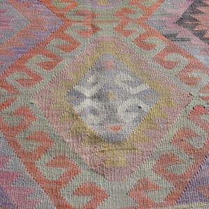K&ouml;nnte beinhalten: Eine Nahaufnahme eines bunten gewebten Teppichs mit geometrischem Muster. Der Teppich ist aus Wolle und hat eine Vielzahl von Farben, darunter Rosa, Rot, Lila und Grau.